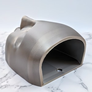 May include: A grey 3D printed planter with a curved, organic shape and a rounded opening. The planter has a smooth, textured surface.