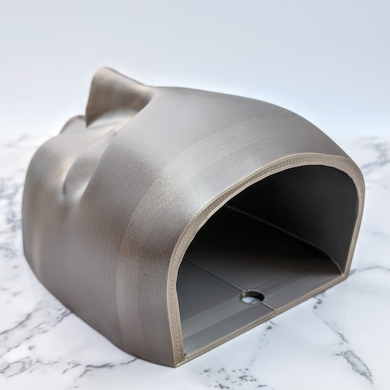 May include: A grey 3D printed planter with a curved, organic shape and a rounded opening. The planter has a smooth, textured surface.