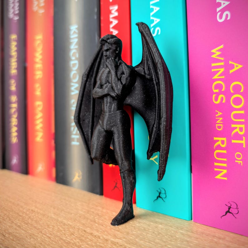 Puede incluir: Una figura negra impresa en tres dimensiones de un ser humanoide alado en una pose contemplativa con una mano cerca de la barbilla. La figura presenta grandes alas texturizadas similares a las de un murci&eacute;lago que salen de la espalda.