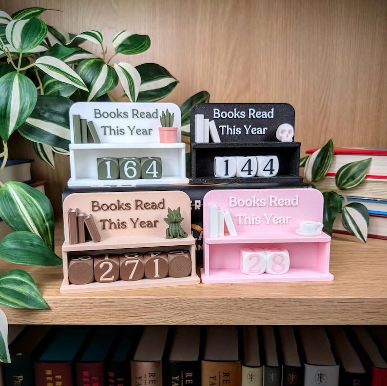 Peut inclure: Quatre pr&eacute;sentoirs miniatures en forme d'&eacute;tag&egrave;res, en blanc, noir, beige et rose. Chaque &eacute;tag&egrave;re affiche le texte "Books Read This Year" et un nombre. Les &eacute;tag&egrave;res sont d&eacute;cor&eacute;es de livres miniatures, d'un cr&acirc;ne, d'un chat, d'une plante et d'une tasse.