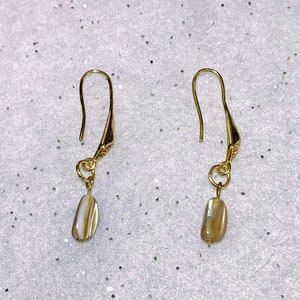 May include: A pair of gold earrings with a white shell-like pendant on each earring.