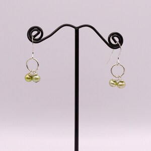 May include: A pair of silver dangle earrings with two green pearl beads on each earring.