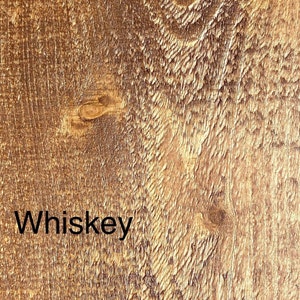 May include: Close-up of a textured, brown wooden surface with the word "Whiskey" in black text. The wood grain has a natural, rustic appearance with knots and variations in color.