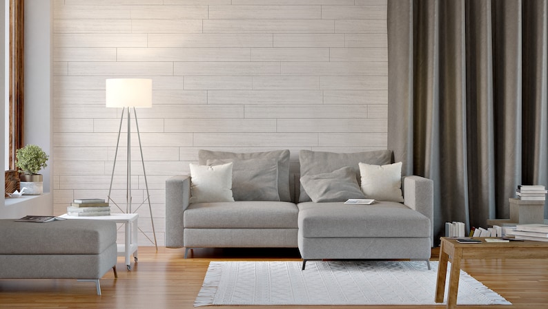 May include: A gray sectional sofa with two pillows sits in a living room with a white wood wall, a floor lamp, and a wooden coffee table.