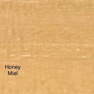 May include: A close-up of a textured, light brown surface. The words "Honey Miel" are printed in black in the lower left corner. The surface has a subtle, natural grain.