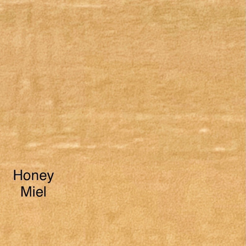 May include: A close-up of a textured, light brown surface. The words "Honey Miel" are printed in black in the lower left corner. The surface has a subtle, natural grain.