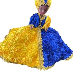 May include: A doll wearing a vibrant, ornate dress and headdress. The dress is split vertically, with one side featuring a yellow rose pattern and the other a blue, ruffled texture. The doll's headdress is yellow with blue jewel accents.