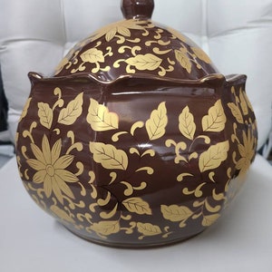 May include: A brown ceramic serving bowl with a lid. The bowl is decorated with a gold floral pattern.