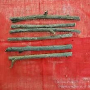 Peut inclure: Huit bâtonnets en bois naturel, d'environ 15 cm de long, de couleur brun clair et de texture rugueuse. Les bâtonnets sont disposés en rangée sur une surface rouge.