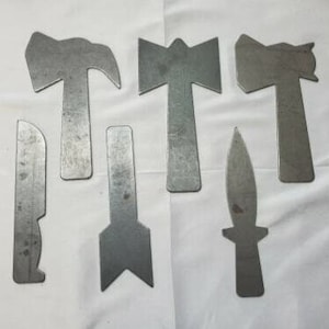 May include: Six metal cutouts in the shape of tools, including a knife, a hammer, and an arrowhead. The cutouts are all made of a silver-colored metal and are arranged in a row on a white surface.