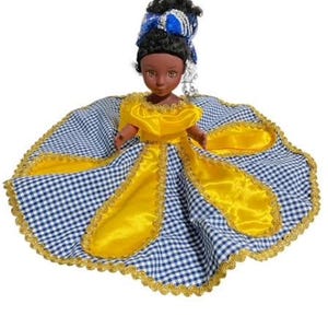 May include: A doll wearing a yellow and blue checkered dress with gold trim. The doll has black hair and brown eyes.