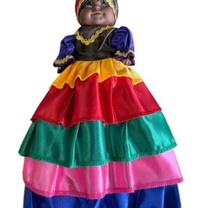May include: A colorful doll with a brown face, black eyes, and a red, yellow, and green turban. The doll is wearing a multi-layered skirt with red, yellow, green, pink, and blue layers.