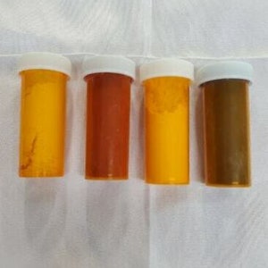 Peut inclure: Quatre petits contenants en plastique transparent avec des couvercles blancs. Les contenants sont remplis de poudres de différentes couleurs : jaune, orange, jaune et marron.