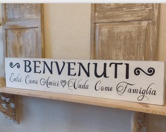 May include: White wooden sign with black lettering that reads "BENVENUTI" and "Entri Come Amici Vada Come Famiglia".
