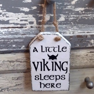 Viking themed Nursery Sign. A little Viking sleeps here. Wood sign, white background, black lettering with Viking helmet. hanging on a rustic painted gray dresser by Jute rope hanger