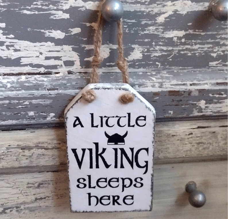 Viking themed Nursery Sign. A little Viking sleeps here. Wood sign, white background, black lettering with Viking helmet. hanging on a rustic painted gray dresser by Jute rope hanger