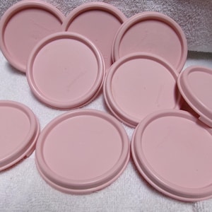 May include: Nine pink plastic lids for containers. The lids are round and have a smooth surface.