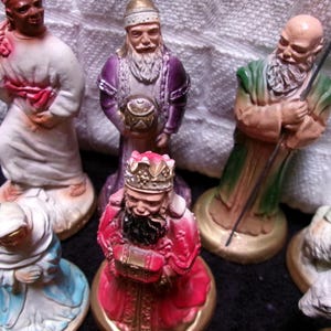 May include: A set of ten nativity figurines, including a shepherd, a king, and a woman holding a baby. The figurines are made of painted plaster and are standing on a white surface.
