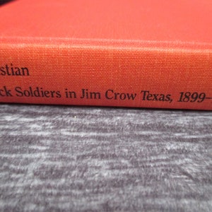 May include: A red book with the title "Christian Black Soldiers in Jim Crow Texas, 1899-1917" on the spine.