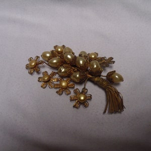 May include: A gold-toned brooch with a cluster of faux pearls and a tassel. The pearls are arranged in a bouquet shape with small gold flowers.