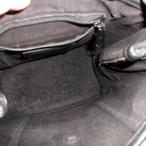 May include: Interior view of a black leather handbag. The bag has a zippered pocket and a dark, textured lining. The top edge of the bag is visible, along with a portion of the brown patterned exterior.