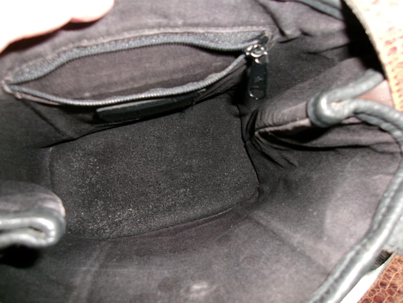 May include: Interior view of a black leather handbag. The bag has a zippered pocket and a dark, textured lining. The top edge of the bag is visible, along with a portion of the brown patterned exterior.
