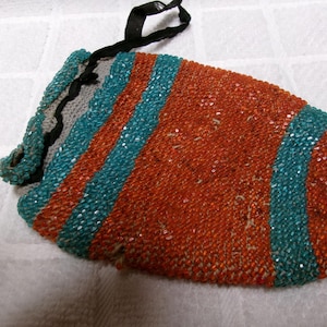 May include: A small, beaded bag with a drawstring closure. The bag is made of orange and teal beads and has a black ribbon handle.