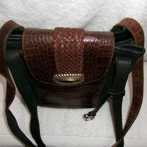 May include: A brown leather crossbody bag with a textured, crocodile-like pattern. The bag features a woven flap closure with a silver-toned clasp and a black leather strap. The bag is approximately 8 inches wide.