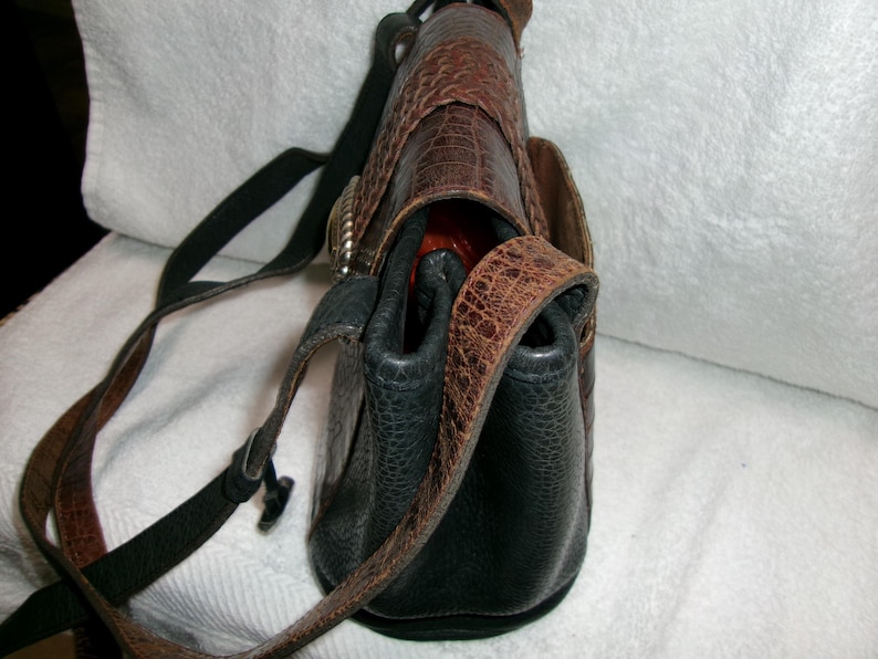 May include: A leather crossbody bag with a textured, reptile-like pattern in shades of brown and black. The bag features a long, adjustable strap and a silver-toned buckle. The interior appears to be a bright orange color.