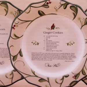 May include: Two decorative plates with floral designs and recipes for Caramel Popcorn and Ginger Cookies. The recipes include ingredients and instructions for making the treats.