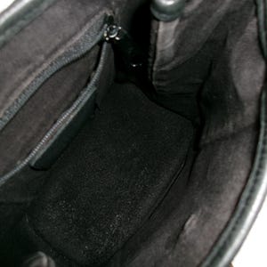 May include: Black leather handbag with an open interior. The inside of the bag is lined with a dark fabric, and a zippered pocket is visible. The bag's interior is spacious, and the leather appears to be in good condition.