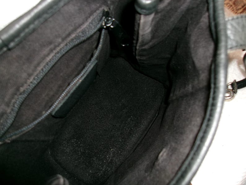 May include: Black leather handbag with an open interior. The inside of the bag is lined with a dark fabric, and a zippered pocket is visible. The bag's interior is spacious, and the leather appears to be in good condition.