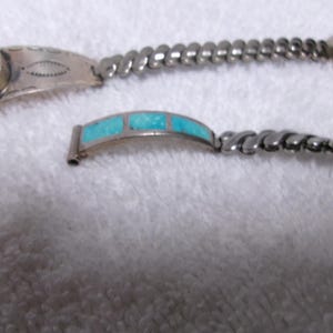 May include: Two silver bracelets with turquoise accents. One bracelet features a bezel-set turquoise stone, while the other has a decorative design. The bracelets have a twisted rope design.