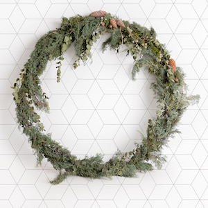 May include: A circular wreath composed of green and brown foliage, including pine needles, eucalyptus leaves, and pine cones. The wreath is set against a white wall with a geometric pattern, offering a natural, rustic aesthetic.