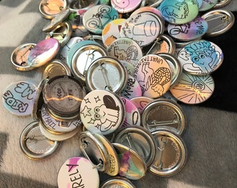 May include: A collection of colourful round button badges with various designs and text, including "I forgot", "Barely", "Ride", "500p", "Catch Me", "Don't Like You Either", and "Unattainable".