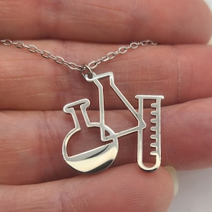 May include: A silver necklace with a pendant shaped like a beaker, flask, and graduated cylinder. The pendant is a simple outline of the lab equipment.