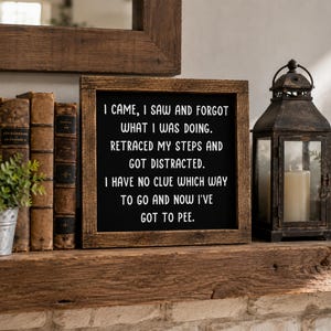 May include: A square wooden sign with a dark brown frame and a black background featuring white text that reads: I CAME, I SAW AND FORGOT WHAT I WAS DOING. RETRACED MY STEPS AND GOT DISTRACTED. I HAVE NO CLUE WHICH WAY TO GO AND NOW I'VE GOT TO PEE.