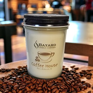 May include: A white candle jar with a brown lid and a gold label that reads "Bayard Candle Company" and "Coffee House" with a small coffee cup graphic. The candle is sitting on a bed of coffee beans.