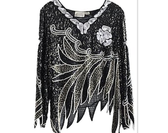 Puede incluir: Una blusa negra de lentejuelas con bordados plateados y dorados. La blusa tiene manga larga y un corte holgado. El bordado presenta un diseño floral con hojas y espirales.