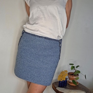 May include: A blue knitted skirt with a white top and a small potted plant on a wooden stool.