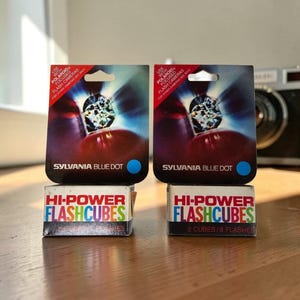 May include: Two boxes of Sylvania Blue Dot Hi-Power Flashcubes. Each box features a graphic of a flashcube emitting light, the text "Use with Polaroid Focused Flash Cameras," and "2 Cubes / 8 Flashes" printed on the white base of the packaging.