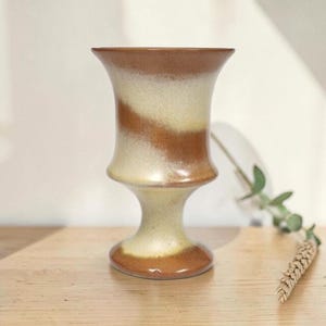 May include: A ceramic goblet featuring a flared rim and a pedestal base. The surface displays a smooth, blended glaze with alternating diagonal bands of warm terracotta brown and creamy off-white, creating a soft, gradient effect throughout.