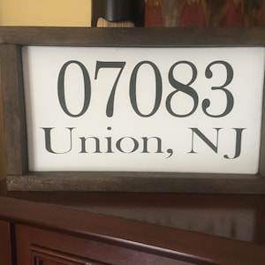 May include: A wooden sign with a white background and black text. The sign reads "07083 Union, NJ".