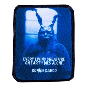 May include: A blue and black embroidered patch featuring a character from the movie Donnie Darko. The character is wearing a rabbit costume and the text "EVERY LIVING CREATURE ON EARTH DIES ALONE. DONNIE DARKO" is printed on the patch.