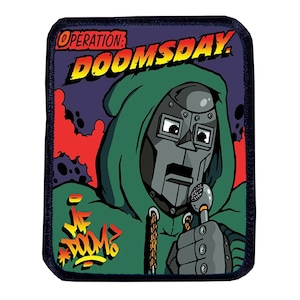 May include: A black and green embroidered patch featuring a cartoon illustration of a superhero wearing a green hooded jacket and a metal mask. The text "OPERATION: DOOMSDAY." is at the top of the patch and the text "MF DOOM" is at the bottom of the patch.