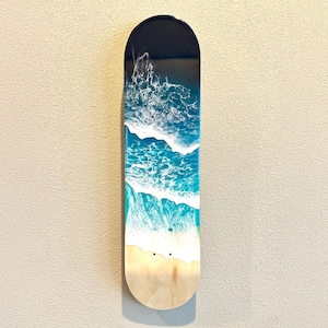 May include: A wooden skateboard deck with a blue and white ocean wave design. The deck is painted with a dark blue background and white foam waves.