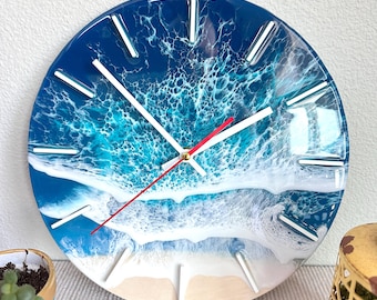 May include: A round resin clock with a blue and white ocean wave design. The clock face has white hour markers and a red and white minute hand.