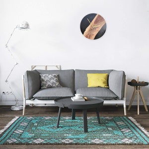 May include: A gray sofa with two pillows, a black coffee table, and a turquoise rug with a geometric pattern. A black and wood clock hangs on the white wall.