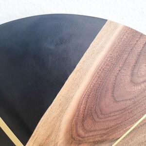 May include: A black and brown wooden clock face with gold accents. The clock face is divided into two sections, one black and one brown. The brown section has a wood grain pattern.