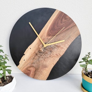 May include: A black and brown wood clock with gold hands. The clock face is divided in half, with one half black and the other half a natural wood grain.
